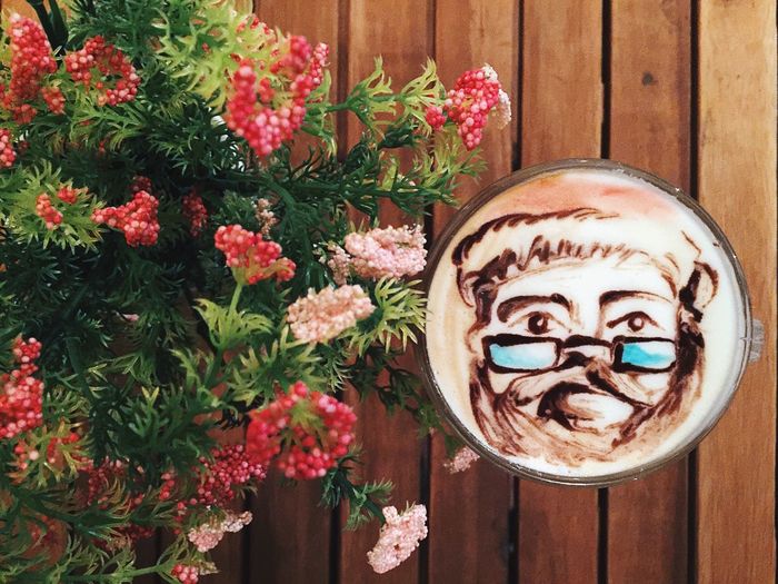 Directly above view of face froth art in latte by flowerpot on table at cafe