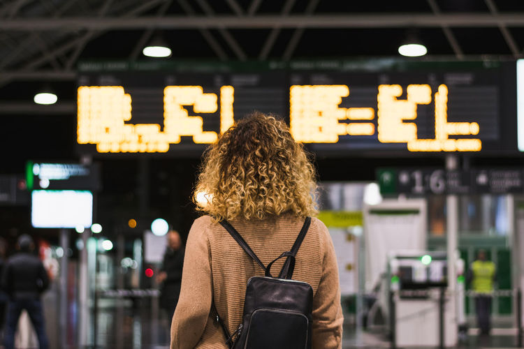 Back view of anonymous female traveler with backpack looking on board with schedule in airport terminal