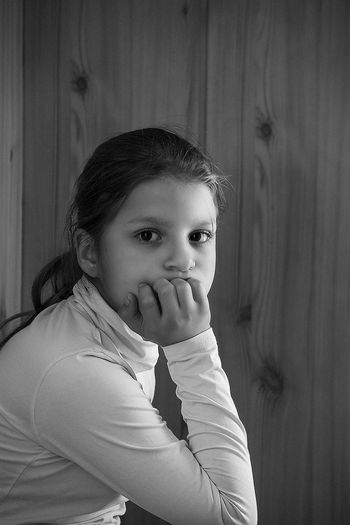 Portrait of girl sitting by wooden wall