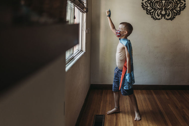 Young boy dressed as super hero with mask standing by window at home