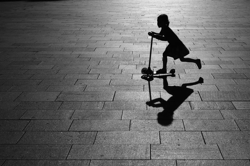 Silhouette of girl riding push scooter on pavement