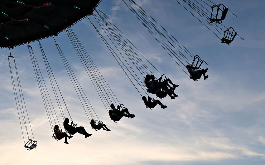 Low angle view of silhouette chain swing ride against sky