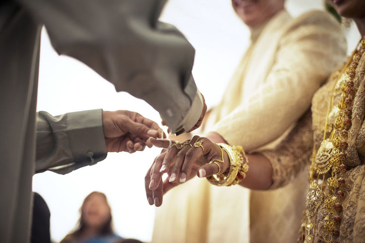 Low angle view of priest tying fingers of bride and groom