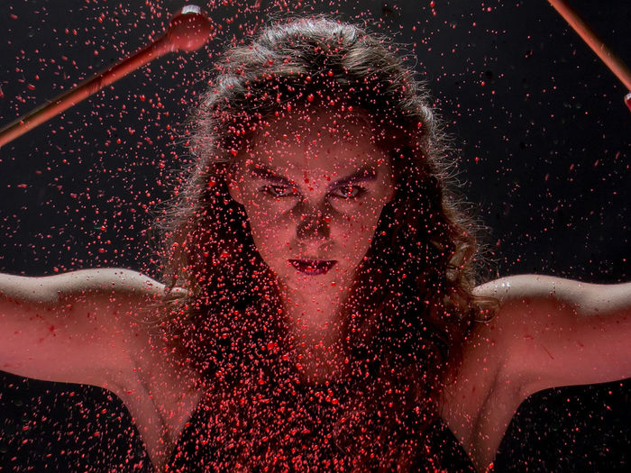 Close-up portrait of young woman seen through red liquid splashing against black background