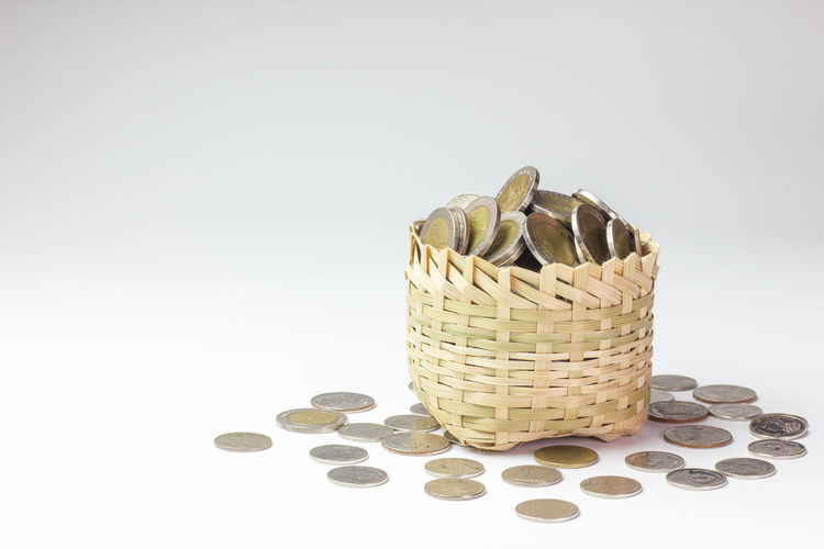 Close-up of coins in basket on table against white background