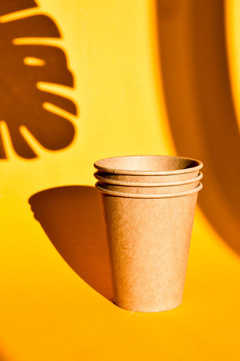 Paper coffee containers on yellow background with hard shadows of palm leaf. paper cups. copy space.