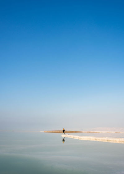 Person standing on beach against clear blue sky