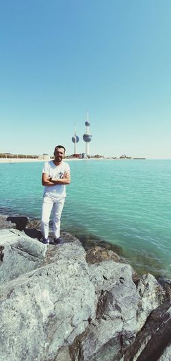 Man standing on rock by sea against clear sky