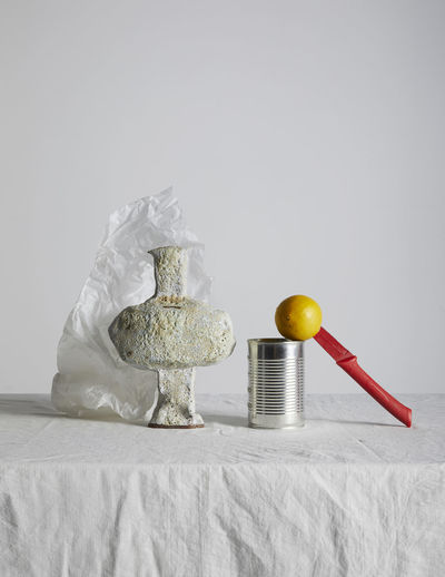 Close-up of stone vase with lemon and knife on table against white background