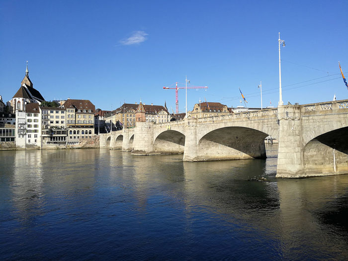 Arch bridge over river by buildings against blue sky