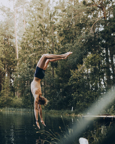 Shirtless man jumping in lake at forest