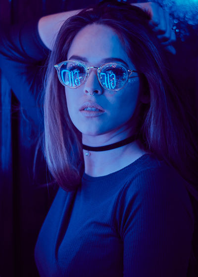 Close-up portrait of young woman wearing sunglasses in darkroom