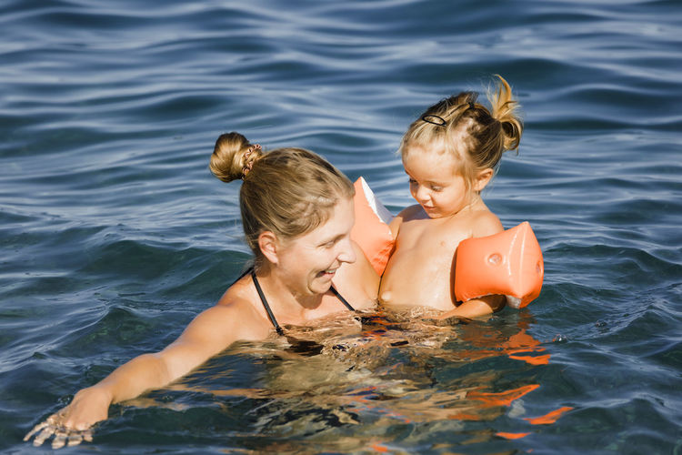 Mother carrying shirtless daughter while swimming in lake