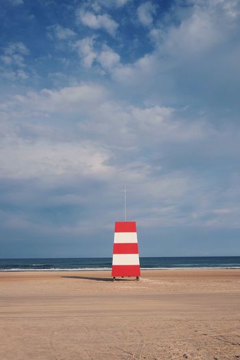 Mid distant view of lifeguard tower at beach against cloudy sky