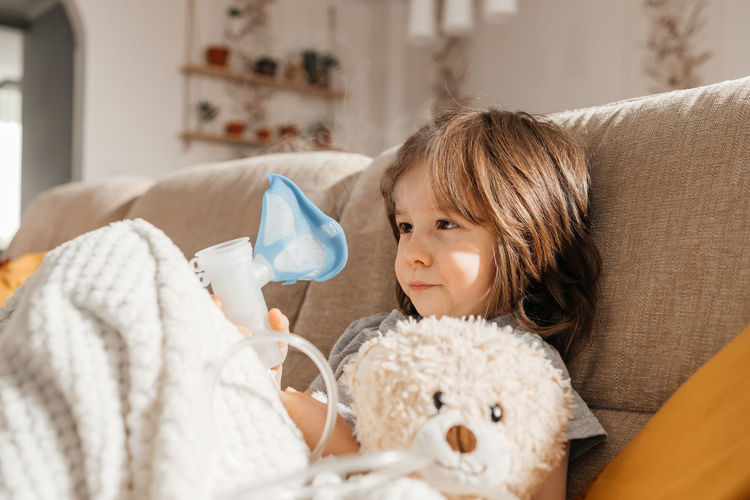 Close-up of a boy doing inhalation at home sitting on the couch with a nebulizer and a mask. 
