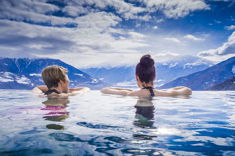 Rear view of friends enjoying in infinity pool against cloudy sky