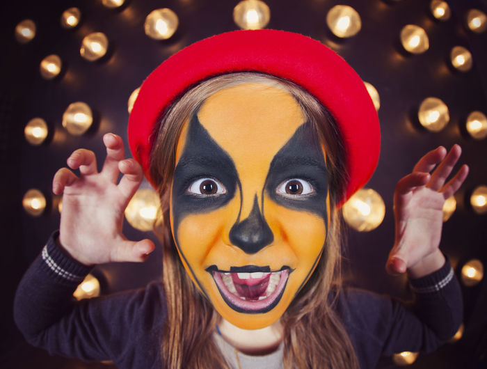 Young woman with face painted against illuminated lights