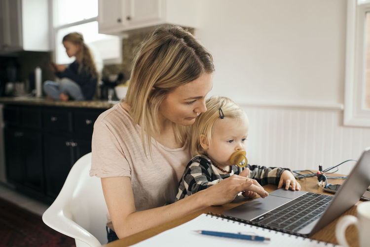 Mid adult woman using laptop while daughter sitting on her lap at home