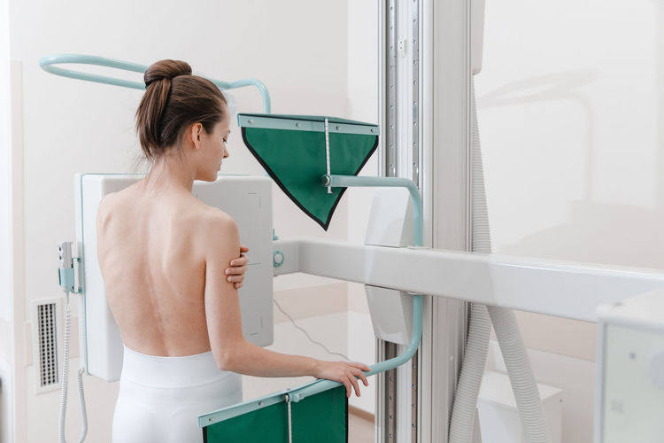 Rear view of shirtless woman scanning chest in clinic