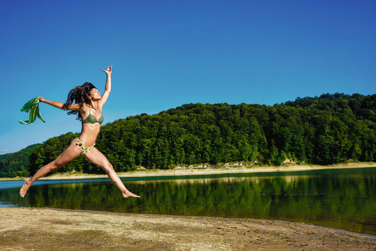 Young woman jumping by lake against sky
