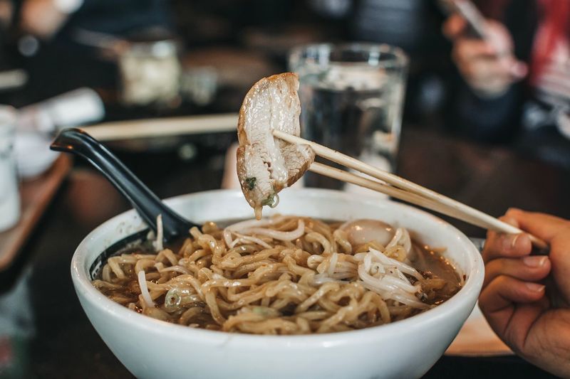 Cropped image of person having noodles soup in restaurant