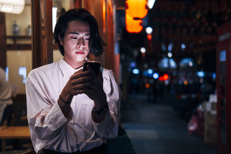 Young man with black hair using smart phone in city at night