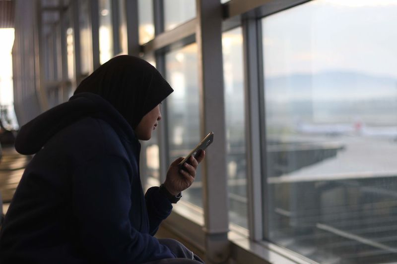 Woman wearing hijab while using mobile phone at airport