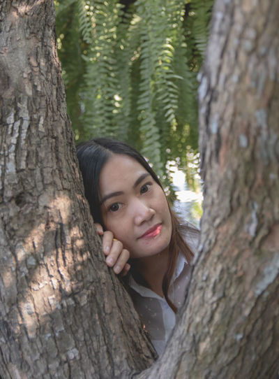 Portrait of woman smiling by tree trunk in forest