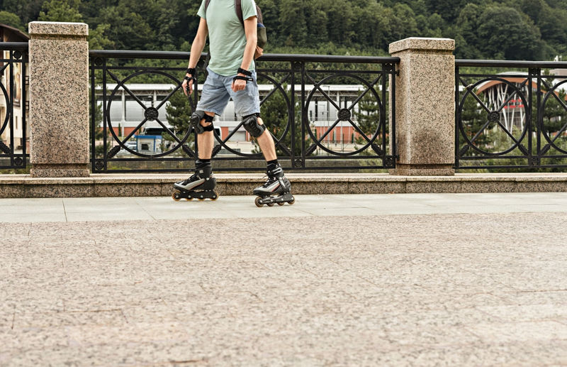 Man in protective equipment riding on roller skates along embankment against background of forest 