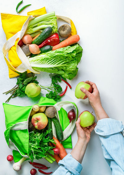 Woman unpacking cotton shopping bags full of fresh vegetables and fruits, top view. healthy eating