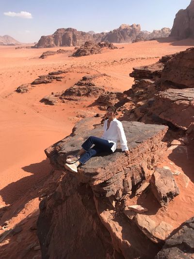 Full length of woman sitting on rock in desert