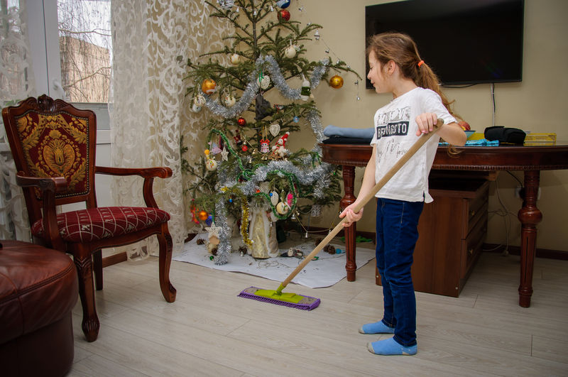 Portrait of man working at home girl 8-9 years old washes the floor  christmas tree