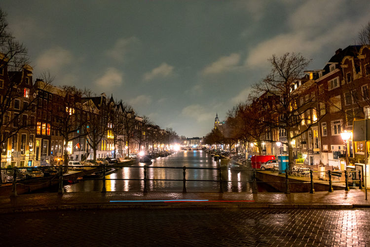 Illuminated buildings by river against sky at night