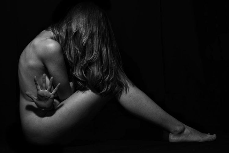 Side view of naked woman sitting over black background