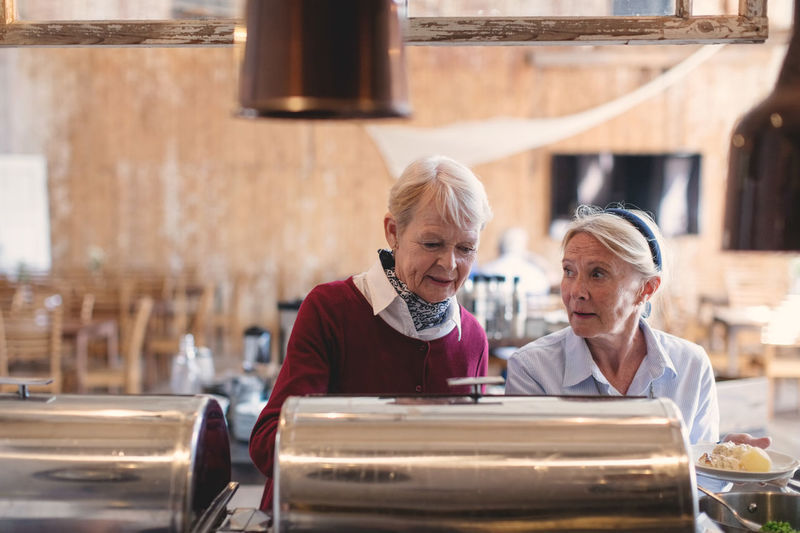 Senior female friends getting food from buffet counter at restaurant