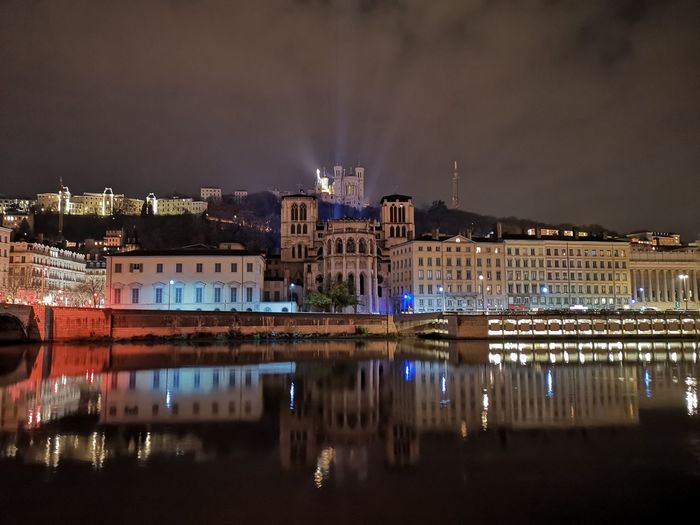 Illuminated buildings by river against sky at night
