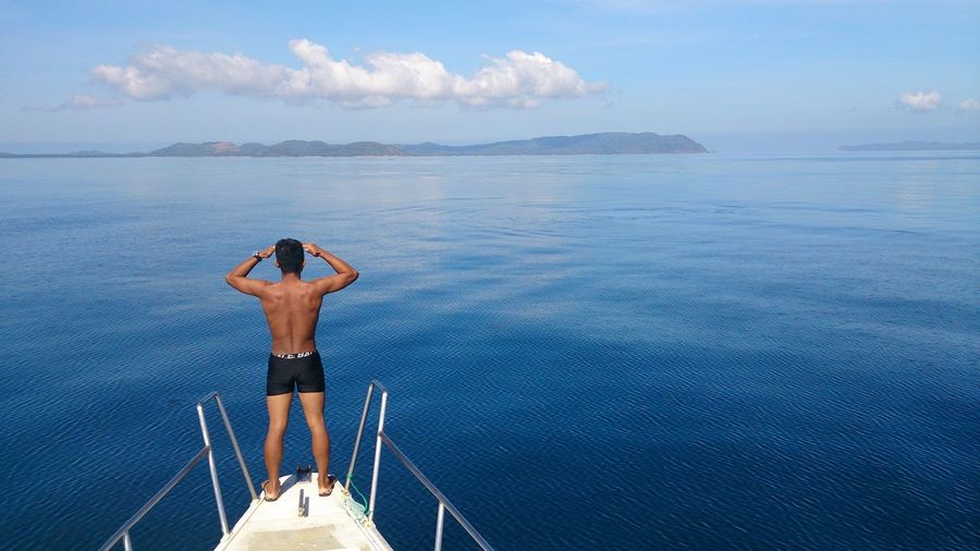 Full length rear view of shirtless man sailing on boat in sea against sky