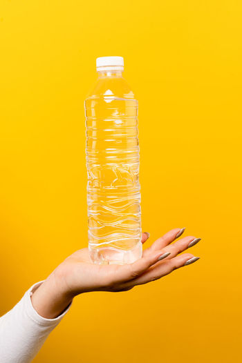 Cropped hand holding bottle against yellow background