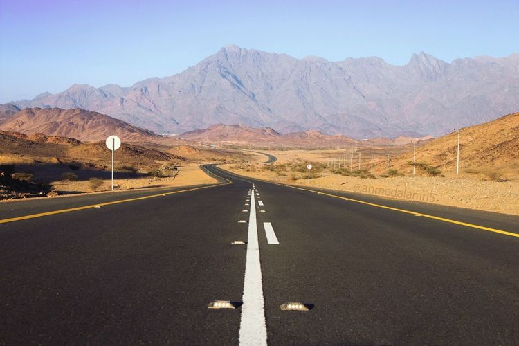 Road leading towards mountains against clear sky