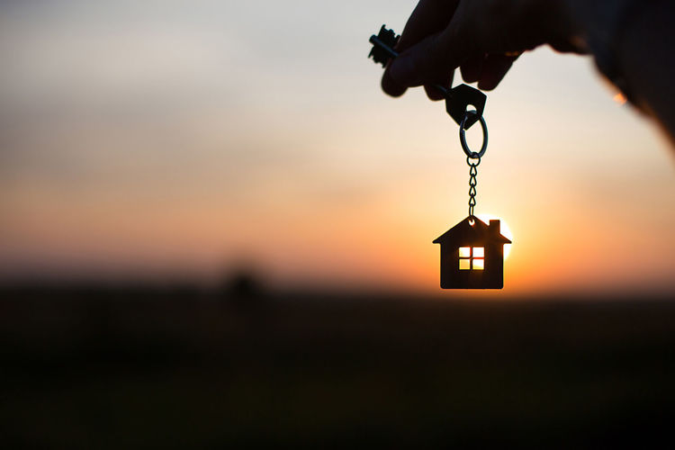 Silhouette of a house figure with a key, a pen with a keychain on the background of the sunset.