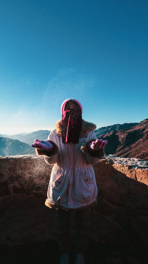 Rear view of woman standing on mountain against clear blue sky