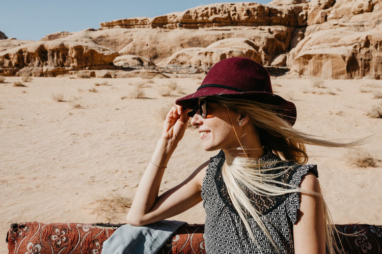 Woman in hat and sunglasses sitting at beach