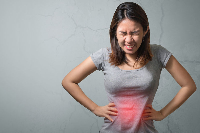 Young woman suffering from stomachache standing against wall