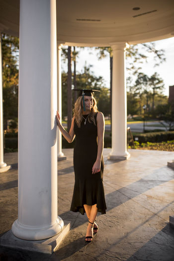College student in courtyard posing by a column with graduation cap