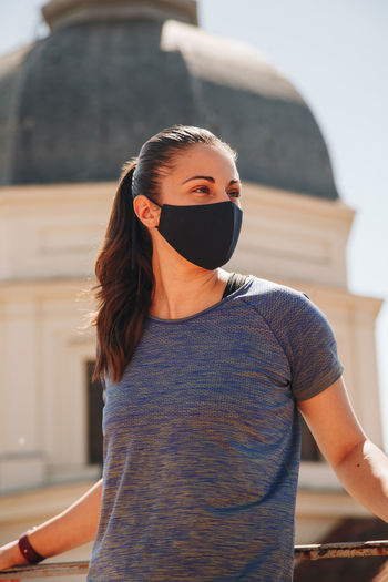 Close-up shot of a young adult female looking forward standing on roof wearing face mask.