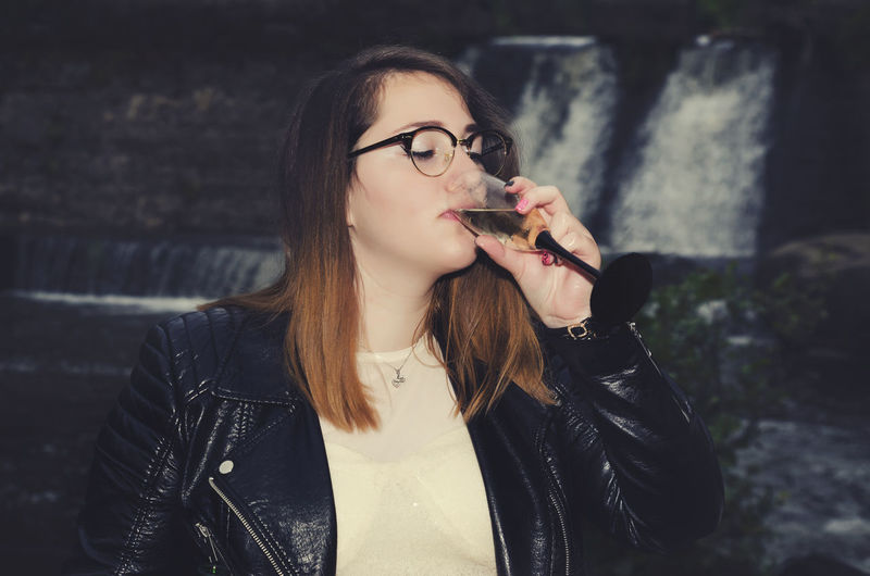 Young woman drinking champagne against waterfall