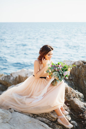 Woman sitting on rock by sea against sky