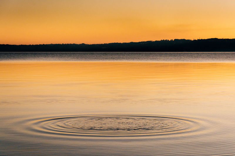Rippled water in lake against clear orange sky during sunset