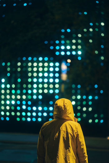 Rear view of man standing against illuminated lights at night