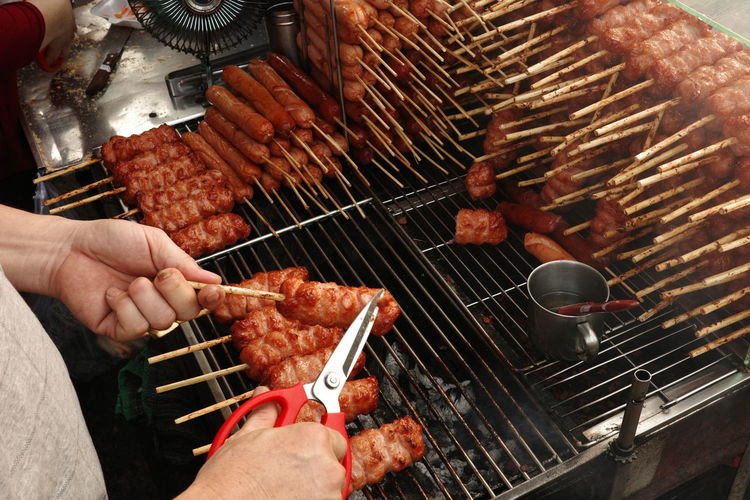 A close-up of a hand using a knife to cut a piece of grilled pork sausage. nem nuong ninh hoa.